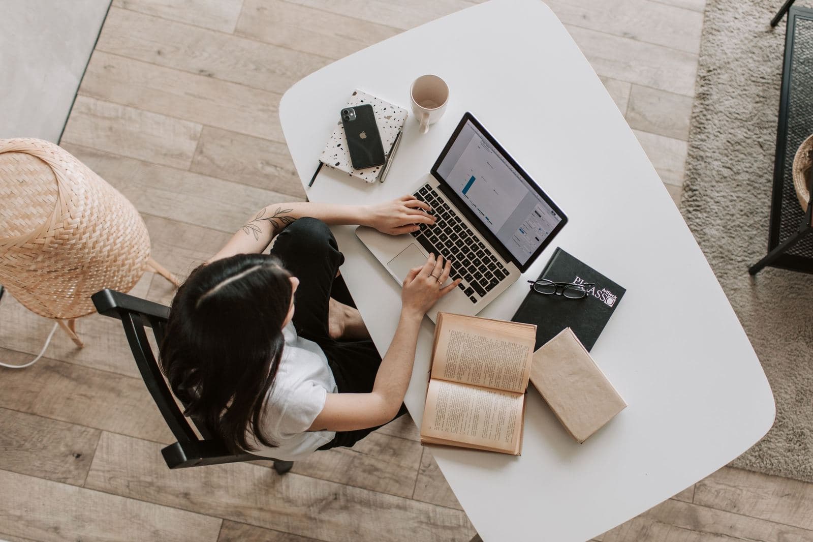 Une femme étudie sur son ordinateur portable, des livres ouverts sur la table.